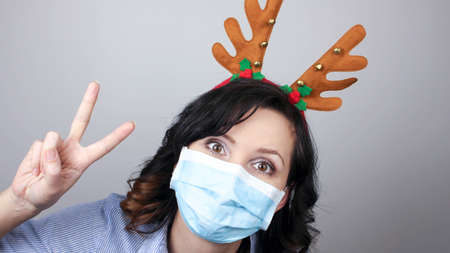 Woman wearing protection face mask against coronavirus. Woman in a mask and deer horns headband. Funny Christmas accessory. Medical mask, Close up shot, Select focus, Prevention from covid19の写真素材