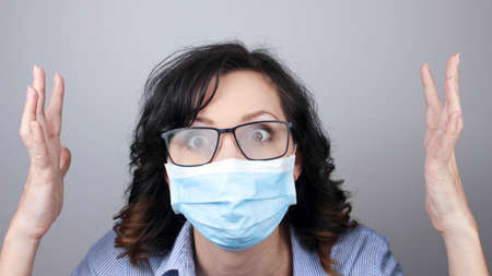 Woman wearing protection face mask against coronavirus and misted glasses. Woman in a mask looking shocked with hands up or worried. Medical mask, Close up shot, Select focus, Prevention from covid19の写真素材