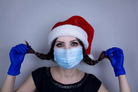 Woman wearing protection face mask against coronavirus. Woman in a mask and Christmas hat. Funny Christmas accessory. Medical mask, Medical gloves, Close up shot, Select focus, Prevention from covid19の写真素材