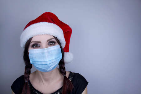 Woman wearing protection face mask against coronavirus. Woman in a mask and Christmas hat. Funny Christmas accessory. Medical mask, Close up shot, Select focus, Prevention from covid19の写真素材