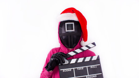 Squid Game pink guard with Christmas hat holding movie clapperboard on white background. Space for text. Red Guard from Squid Game of new Netflix show. Gatineau, Quebec Canada - November 2, 2021のeditorial素材