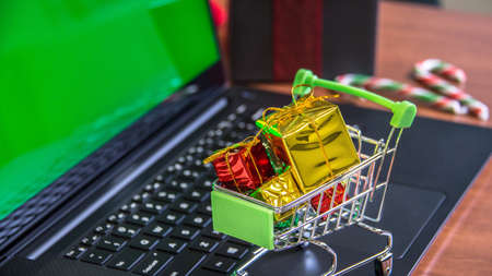 Shopping cart full of christmas gifts on laptop computer with green screen. Online shopping, e-commerce and worldwide shipping concept. Mockup, space for text.の写真素材