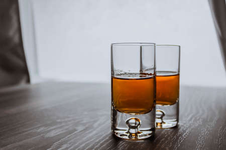Two shot glasses with whiskey on a wooden background table next to window. Space for text.の写真素材