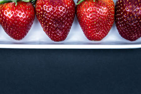 Strawberry in a white plate close up on a black background. Fresh red strawberry in white bowl on black background. side view, copy space, close up.の写真素材