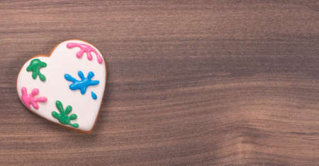 Colorful heart shaped glazed cookie for Valentine's day on wooden background. Paint splatter. Space for text. Easter cookie.の写真素材