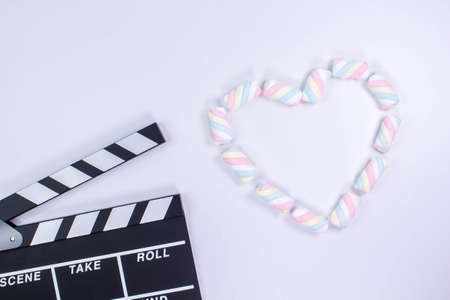 Movie clapperboard with heart shaped from twisted marshmallows. Valentine's day concept. Love. White background with twisted marshmallow pattern. Mock up. Space for text.の写真素材