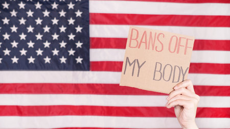 Woman holding a sign My Body, My Choice American flag on background. Protest against anti abortion...