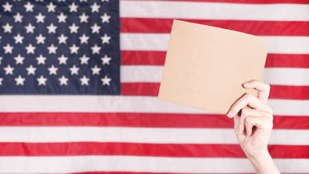 Young woman holding blank sign in her hands close up. American flag on background.の写真素材