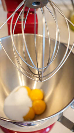 Close up view yellow eggs in a metal mixer bowl. Red stand mixer with white background.の写真素材