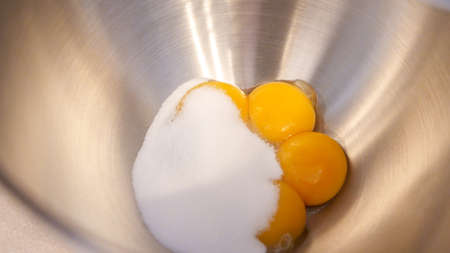 Raw eggs with sugar in a metal bowl of standing mixer. Preparing egg yolk with sugar in kitchen mixerの写真素材