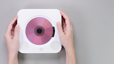 Hands holding stylish white portable compact CD player with pink cd disc playing music on grey background. Retro vintage trending disc player. Top view, space for text. Hobby entertainment leisure.の写真素材