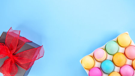 Easter pastel background with colorful eggs and a gift box with red bow on a blue background. The...