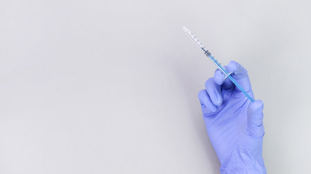 Hand in blue gloves of doctor or nurse holding syringe with liquid vaccine over grey background with copy space. New vaccine. Unknown vaccine. Medical glovesの写真素材