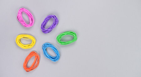 Multicolored abstract triangle figure made of elastic. Top view of colorful rubber bands isolated on grey. Rainbow elastic rubber bands on white. Rainbow flower shapeの写真素材