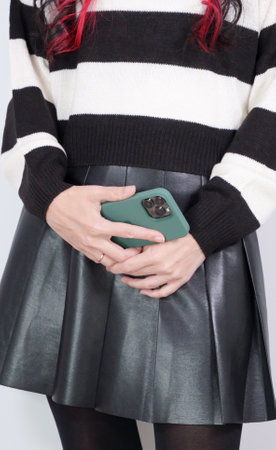Teenager girl in a white and black sweater and leather skirt is using smart phone. Faceless, vertical. Social media, music, testing, online shoppingの写真素材