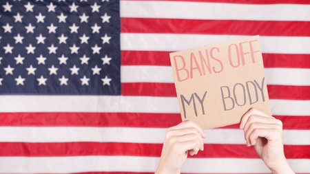 Woman holding a sign Bans Off My Body American flag on background. Protest against anti abortion law. Women's strike. Womens rights freedomの写真素材