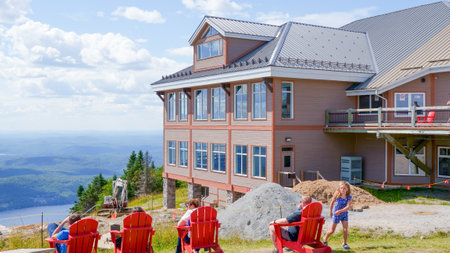 Sightseeing mountain views at Mont Tremblant ski Resort in summer. Tourists enjoying sitting at red chairs at ski resort village. Mont-Tremblant, Quebec, Canada - 22.09.2022のeditorial素材