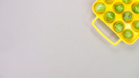 Raw organic Brussel sprouts in yellow container on grey background, top view. Flat lay, overhead,...