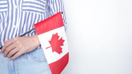 Unrecognized girl student in white blue shirt holding small Canadian flag over gray background, Canada day, holiday, vote, immigration, tax, copy spaceの写真素材