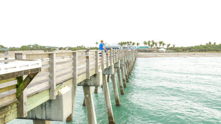 Person fishing at the end of a wooden dock extending into calm blue ocean waters Jacksonville, Florida USA 03.15.2024のeditorial素材