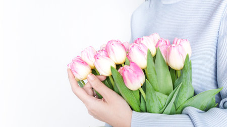 Woman holding vibrant pink tulips bouquet with green foliage on white background