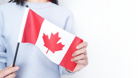 Unrecognized girl student in white blue shirt holding small Canadian flag over gray background, Canada day, holiday, vote, immigration, copy spaceの写真素材