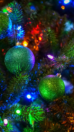 This image features a stunning Christmas tree adorned with green glitter balls and colorful lights against a dark background, perfect for holiday designs, cards, and festive projects.の写真素材