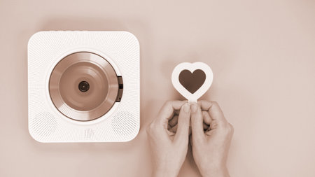 Hands holding white cd player and heart shape gift card on brown background. Colour of the year Mocha Mousse. Love music, Valentine day, Greetingの写真素材