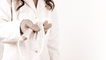 Close-up of doctor's hand holding a medical face mask, on white background.の写真素材