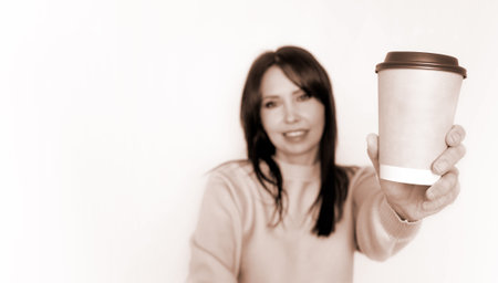 Smiling woman holding up a brown coffee cup with a solid white background.の写真素材