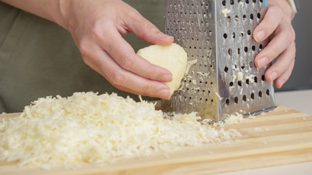 chef grating traditional mozzarella cheese with steel grater on the wooden board.の写真素材