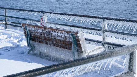 A beautiful wooden bench, adorned with glistening icicles, sits elegantly by the sea. Surrounded by soft, white snow and sparkling ice, it creates a peaceful winter scene, inviting quiet reflection.の写真素材