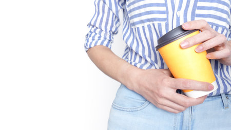 Woman holding a yellow mockup coffee cup with a black lid in front of her lower abdomen.の写真素材