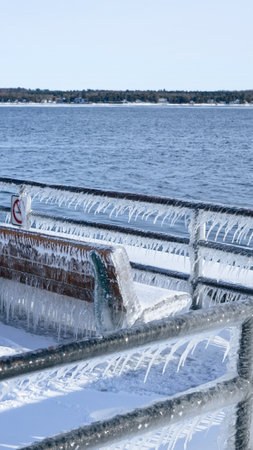 A beautiful wooden bench, adorned with glistening icicles, sits elegantly by the sea. Surrounded by soft, white snow and sparkling ice, it creates a peaceful winter scene, inviting quiet reflection.の写真素材
