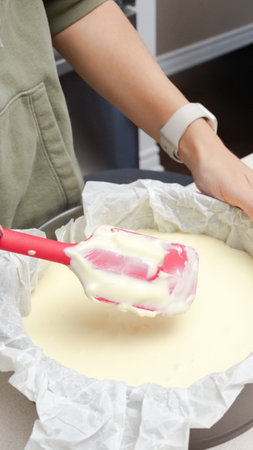 Deliciously Smooth Cake Batter Being Mixed with a Red Spatula in a Black Round Cake Pan.の写真素材