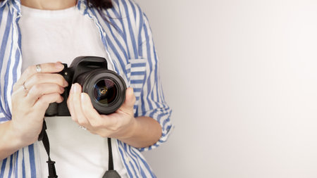 Photographer holding dslr camera. Self portrait, front view. Faceless nice woman with brown red hair in a tshirt with hands holding photo camera white backgroundの写真素材