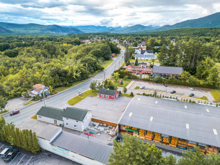 This stunning aerial view captures a charming town nestled among majestic mountains. Lush green forests surround the area, with a clear blue sky and fluffy clouds enhancing the beauty.の写真素材
