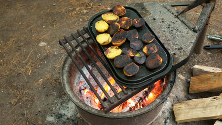 A close-up of rustic potatoes cooking on a campfire grill grate, highlighting their charred and crispy exterior while revealing the soft and fluffy interior, perfect for outdoor cooking enthusiasts.の写真素材