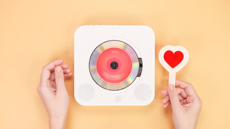 A vintage white retro styled portable compact disc player sits next to a vibrant red heart-shaped object, beautifully isolated on a soft peach background, creating a nostalgic and romantic atmosphere.の写真素材