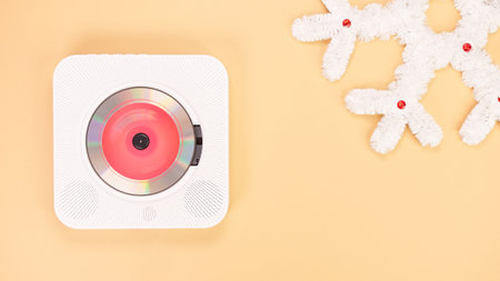 A white portable CD player is positioned on a beige background next to a decorative white snowflake made of tinsel.の写真素材