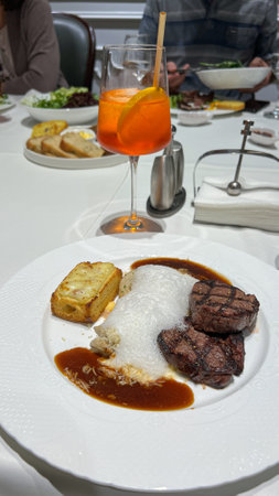Savor a gourmet steak dinner with tender cuts, cheesy potato gratin, and rich sauce, paired with a refreshing Aperol Spritz. Ideal for food blogs and restaurant promotions.の写真素材
