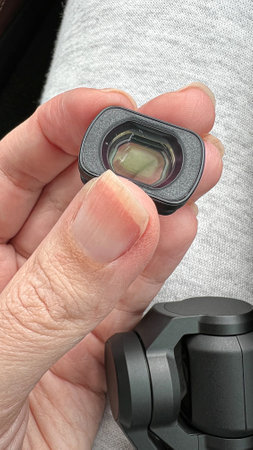 Close-up of a hand holding a small scratched camera lens, highlighting precision optics and technology. Perfect for themes in photography, videography, and modern advancements in creative projects.の写真素材