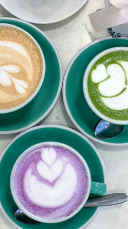 Savor these three exquisite coffee an d matcha drinks adorned with colorful latte art. Perfect for a cozy cafe setting, they offer a delightful experience for coffee lovers and social gatherings.の写真素材