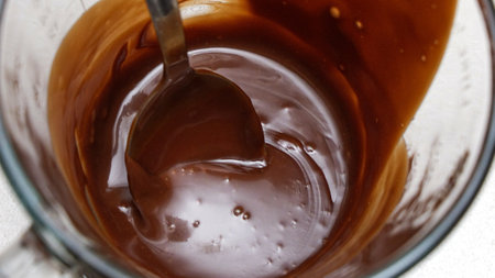 Close-up of a milk chocolate ganache in a glass measuring cup with a spoon.の写真素材