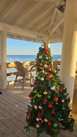 A vibrant array of baubles decorates a festive Christmas tree on a beachfront deck, with the ocean as a backdrop, creating a cheerful holiday ambiance for Christmas celebrations.の写真素材