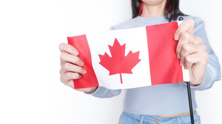 Unrecognized girl student in white blue shirt holding small Canadian flag over gray background, Canada day, holiday, immigration, copy space.の写真素材