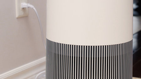 Tall round air purifier with a black top fan and a white body on a tile floor against the wall.の写真素材