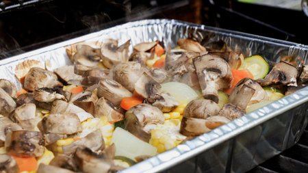 A foil pan filled with fresh vegetables like mushrooms, zucchini, carrots, and corn, grilled outdoors. A healthy and delicious option for summer cookouts and barbecues.の写真素材