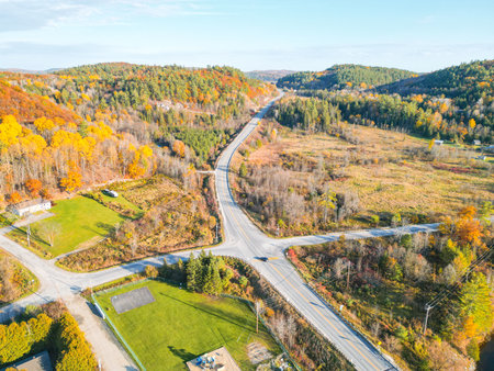 The image shows a beautiful rural landscape with a road in the center. The road is surrounded by colorful autumn trees and there is a blue sky with white clouds in the background.の写真素材