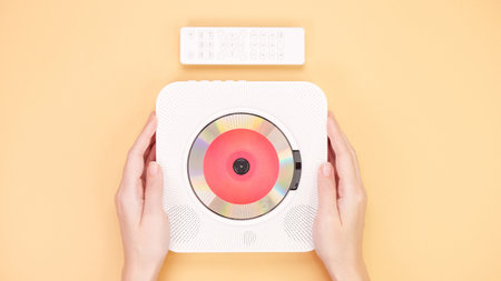A sleek, white CD player positioned elegantly on a soft peach background. The player comes with a compact remote control, highlighting its portable design for easy audio playback and convenience.の写真素材